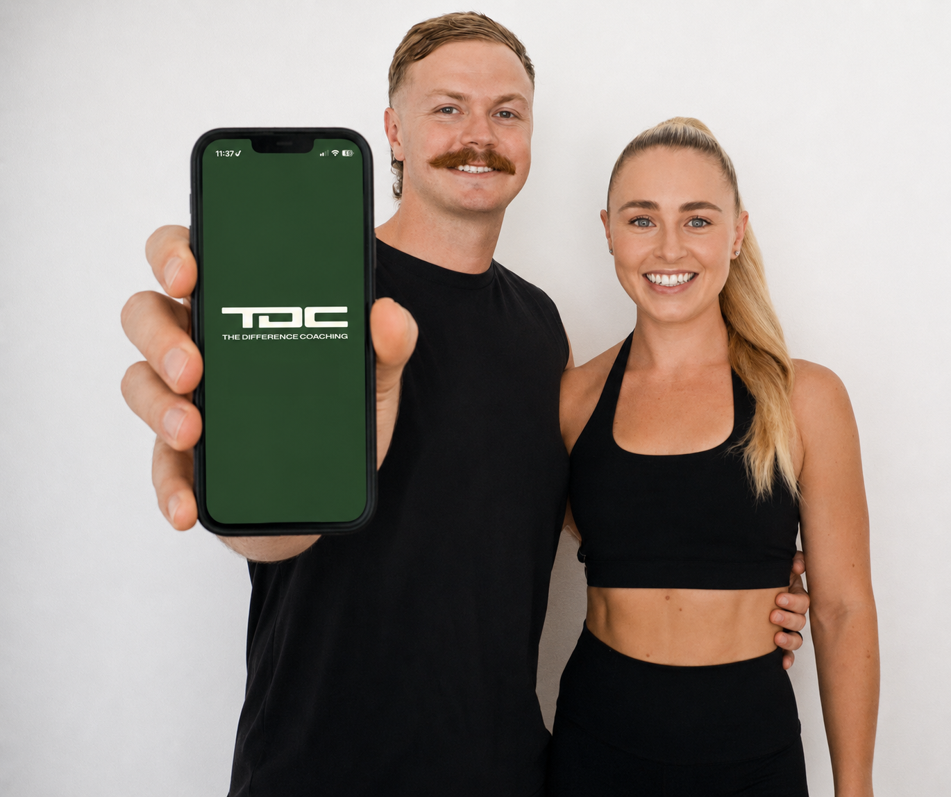 A man and a woman in activewear, the man holding a phone showing the TDC logo